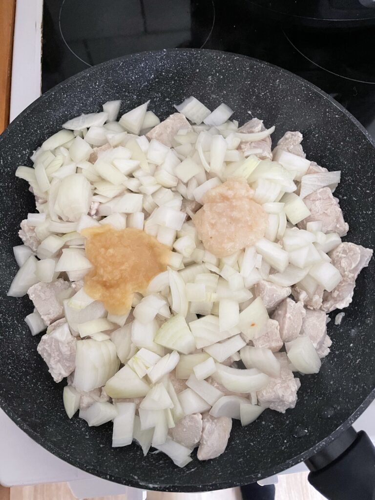 Diced Chicken in a frying pan with onions, minced garlic, and minced ginger.