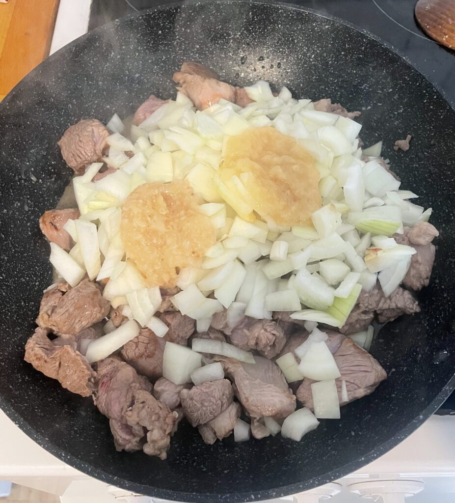 Lamb, onions, minced ginger, and minced garlic in a frying pan